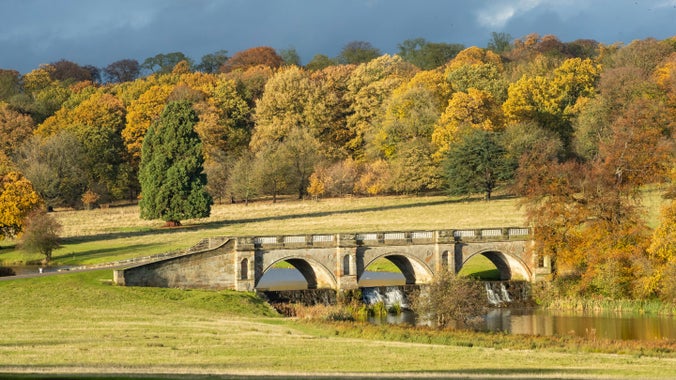 Autumnal view of the 18th century bridge and woodland beyond at Kedleston Hall, Derbyshire
